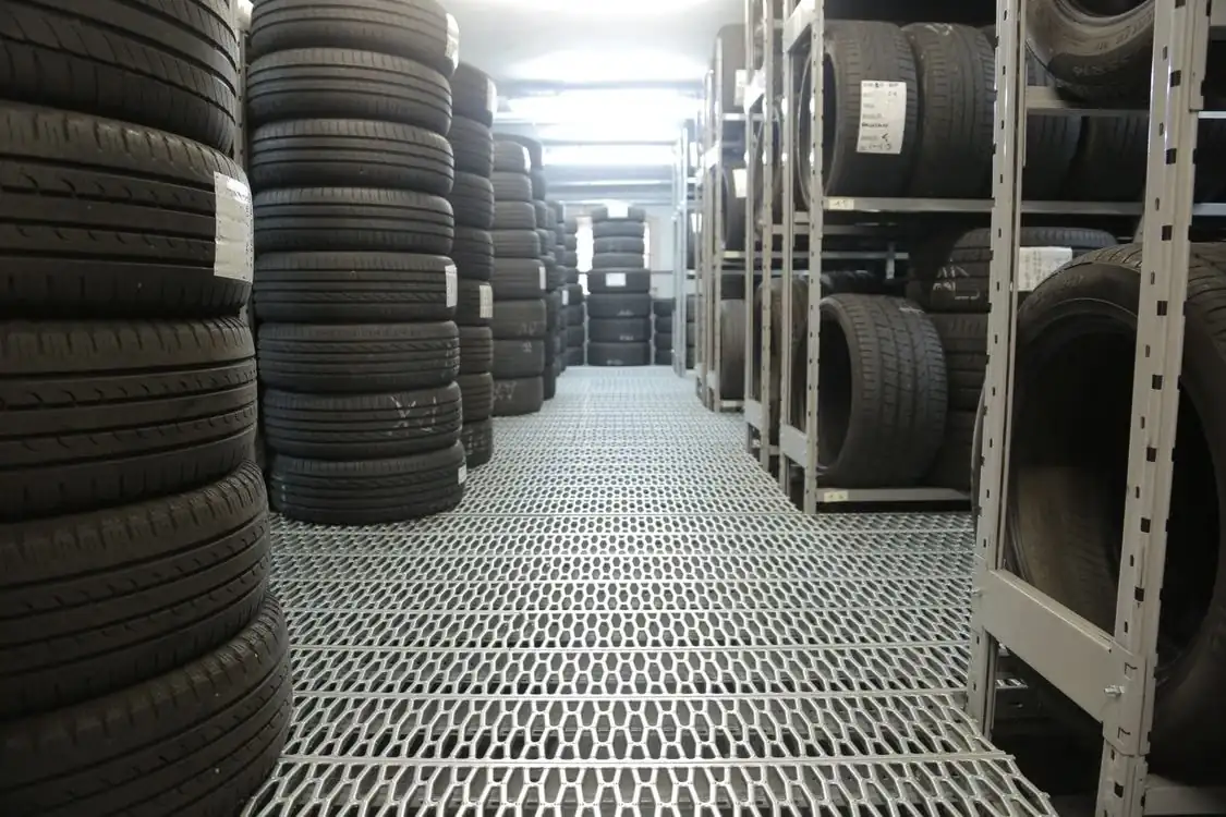 Illustrative photo of an automotive tyre storehouse, with tyres stacked beside metal storage racks. Location not specified by the source.